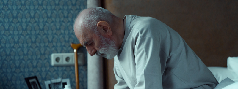 Older man sits on edge of bed